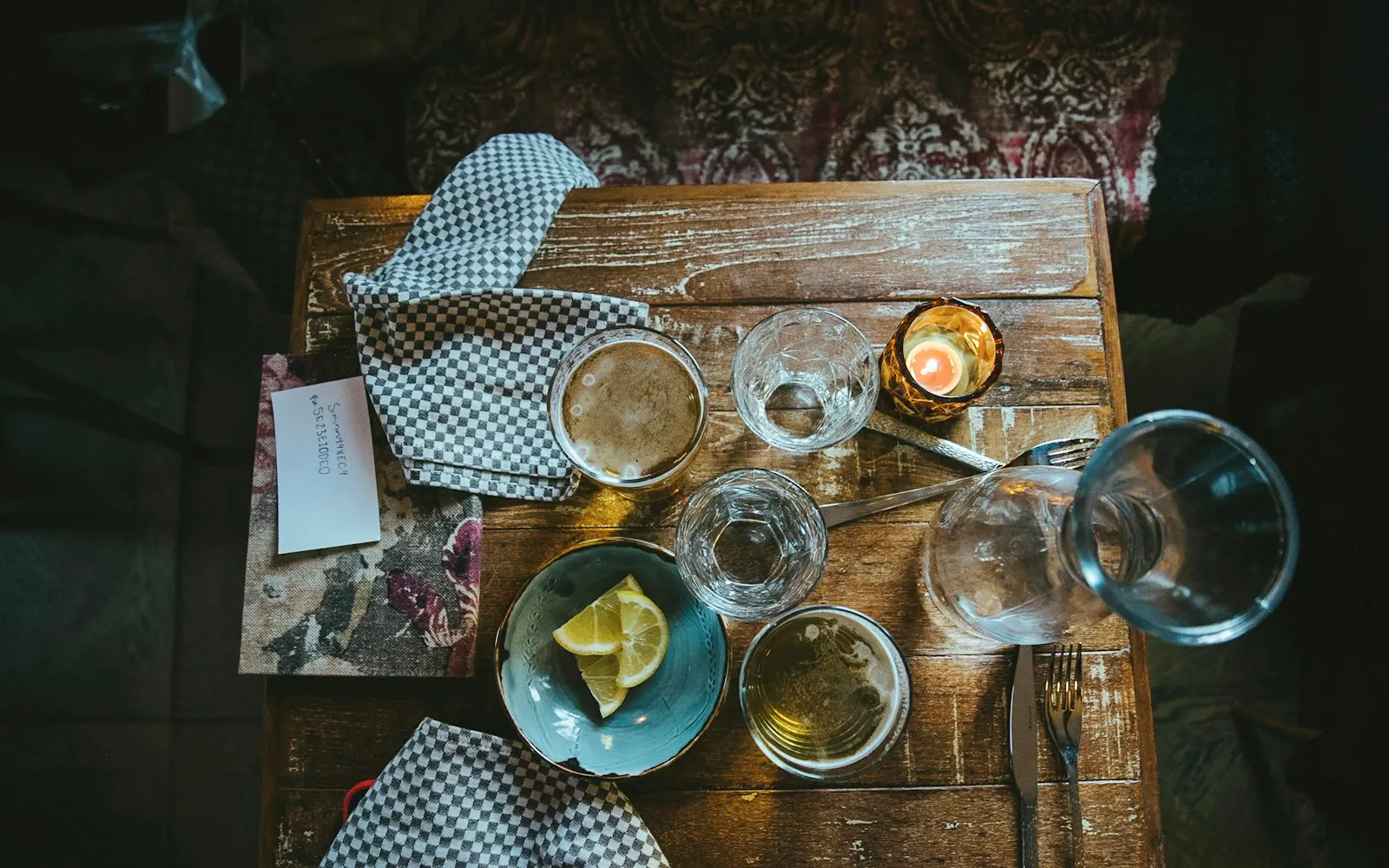 La tavola a fine pranzo, dall'alto: tovaglioli a scacchi, bicchieri, una candela